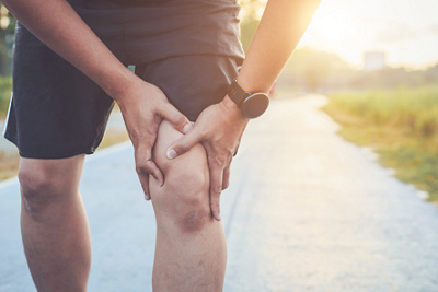 Injury from workout concept : Asian man use hands hold on his knee while running on road in the park. Shot in morning time, sunlight and warm effect with copy space for text or design, Injury from workout concept : Asian man use hands hold on his kn