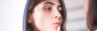 Woman applying cold sore cream on lips in front of mirror