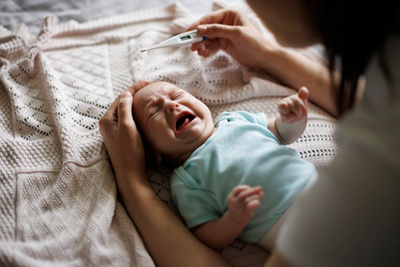 Mother checking her son’s temperature with her hand and a thermometer