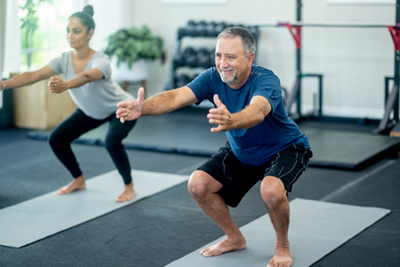 älterer Mann und junge Frau auf Fitnessmatte im Squat