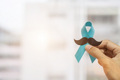 Movember turquoise headband with mustache held by one hand on a light background
