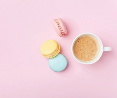 Cup of coffee and colorful macaron on pastel pink background top view. Cozy breakfast. Fashion flat lay. Copy space for text.