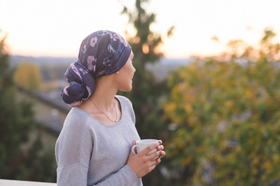 Chemopatientin mit Kopftuch blickt mit Kaffee in die Ferne