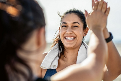 Smiling woman giving high five to her friend after exercising. Woman looking happy after a successful workout session outdoors.