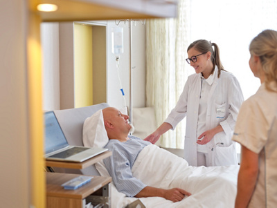 hirslanden-patient-in-bett-besprechung-aerztin-pflege