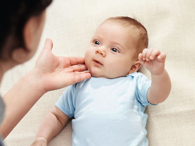 Baby liegt auf Decke und schaut zur Mutter hoch