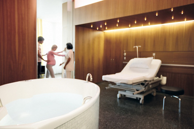 Frau in den Wehen im Gebärsaal mit  Badewanne und Bett