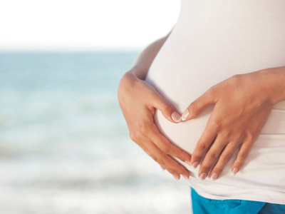 Eine schwangere Frau formt mit ihren Händen ein Herz über ihrem Bauch