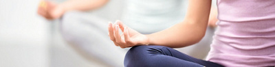 Ausschnitt vom Oberkörper einer Frau, die Yoga praktiziert und die Hand auf dem Knie aufgelegt hat