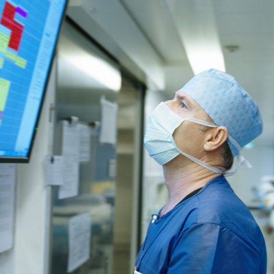 Ein Mann mit chirurgischer Maske schaut einen Plan auf einem Bildschirm.