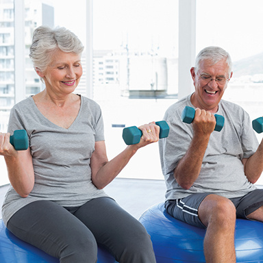 Happy senior couple sitting on fitness balls with dumbbells in the medical office