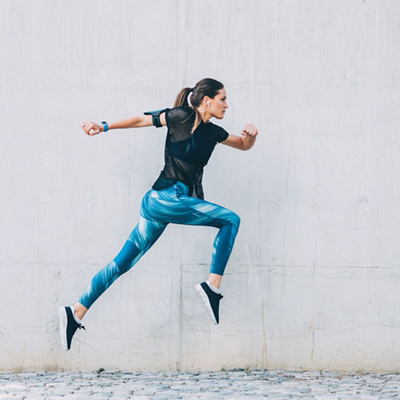 Sportswoman jumping in front of a wall outdoors.