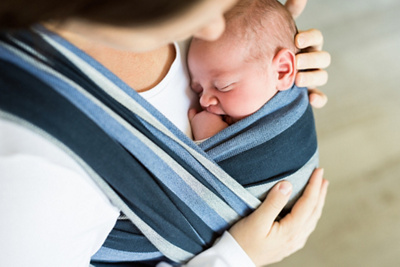 Close up of unrecognizable young mother with her newborn baby son in sling at home