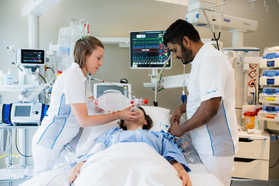 Eine Dipl. Expertin und ein Dipl. Experte Intensivpflege NDS helfen einer Patientin auf der Intensivstation in einer Notfallsituation.